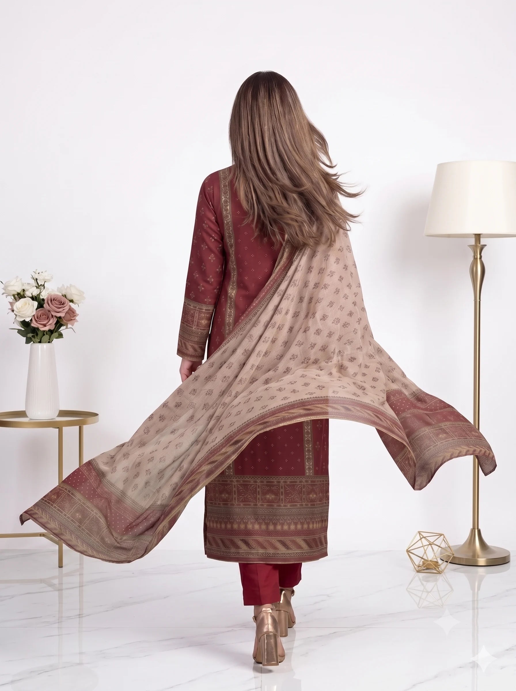 Woman wearing a maroon and beige traditional outfit with a flowing scarf in a minimalistic room.